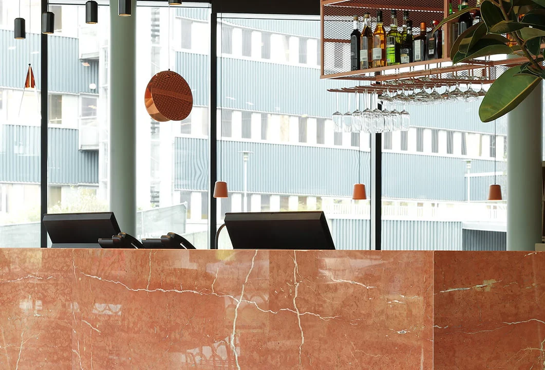 Receptionen på hotellet Grow Hotel. Marmordisk, två datorskärmar syns. Från taket hänger en designerlampa och en hylla med flaskor. Från den hänger i sin tur vinglas.